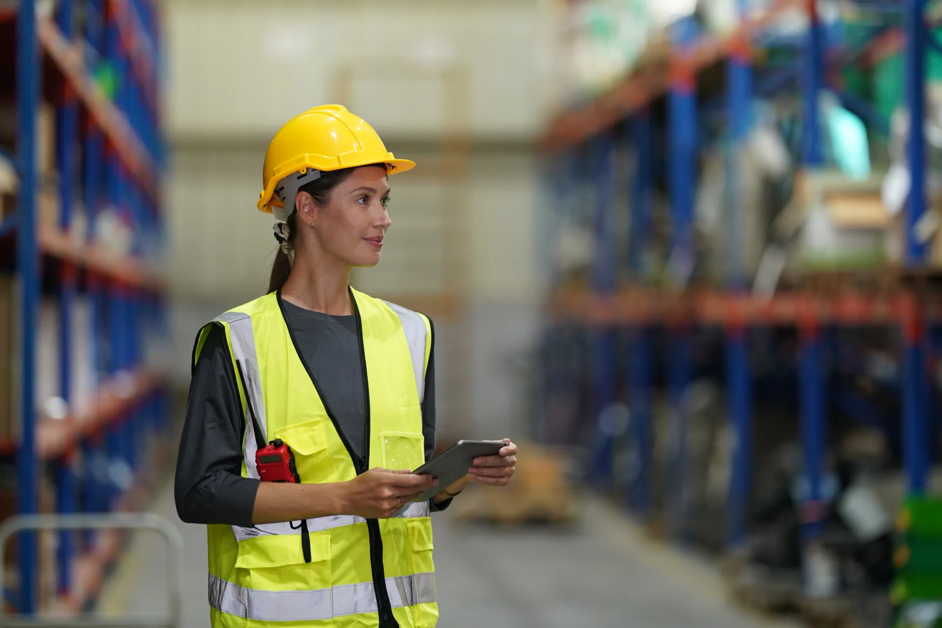 Supervisor in a hard hat and high-visibility vest walking through the warehouse with a tablet